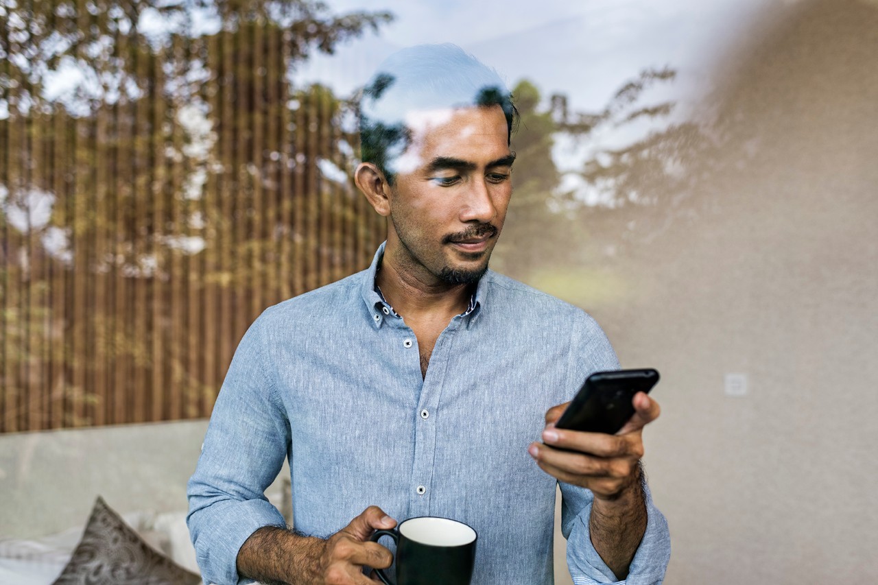 A man looking at his phone while drinking his coffee